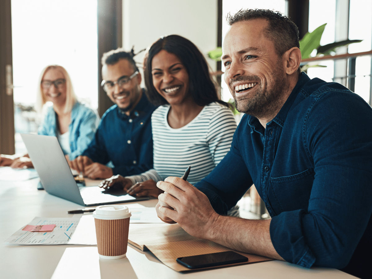 Four coworkers lined up at a conference table smiling and collaborating on email archive migration